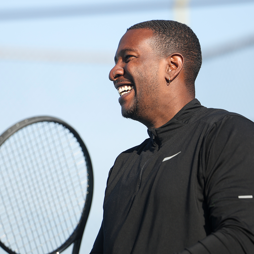 Black male tennis player smiling while holding a tennis racket in Southern California.