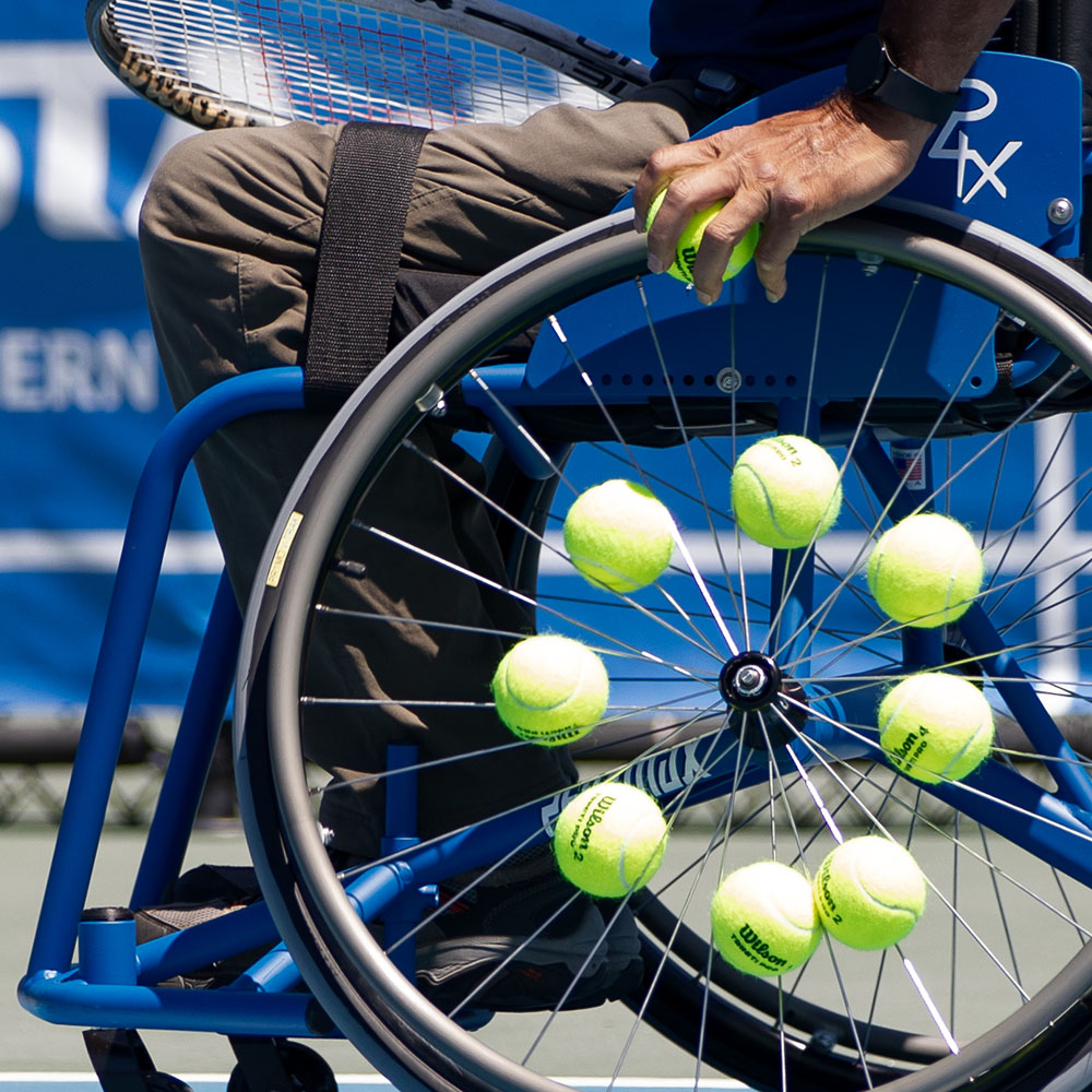 Close up image of a wheelchair with tennis balls in the spikes.