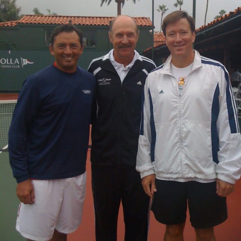 Fred Guerra, Stan Smith, and Ray Wells smiling on a tennis court together in Southern California.