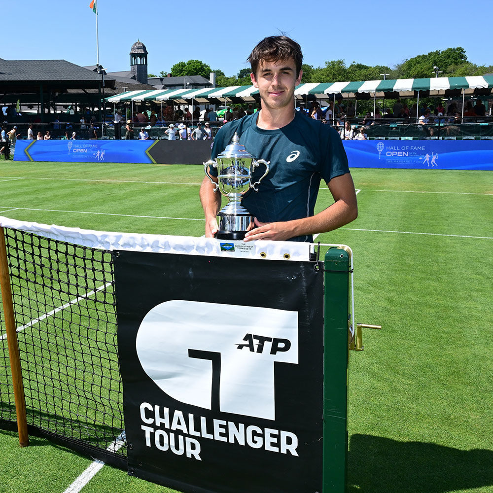 Zach Svajda smiles with his trophy in front of the ATP Challenger court sign after winning the singles title at the Hall of Fame Open in Newport.