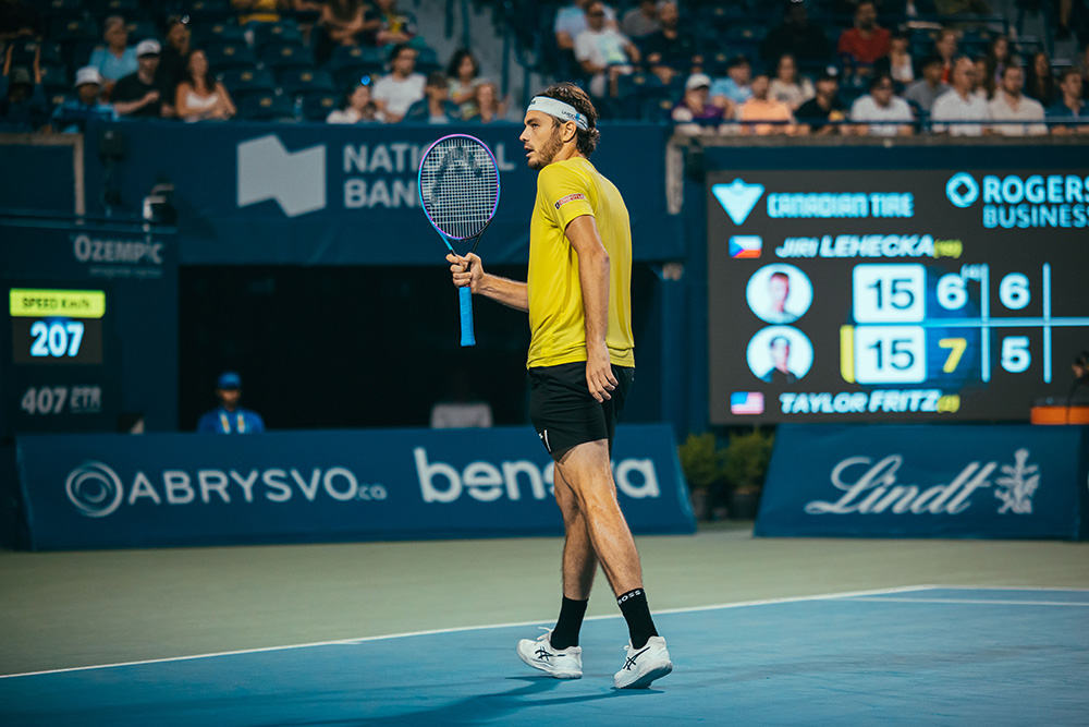 Taylor Fritz waves his tennis racquet celebrating a point while wearing bright yellow and black at the Canada Open