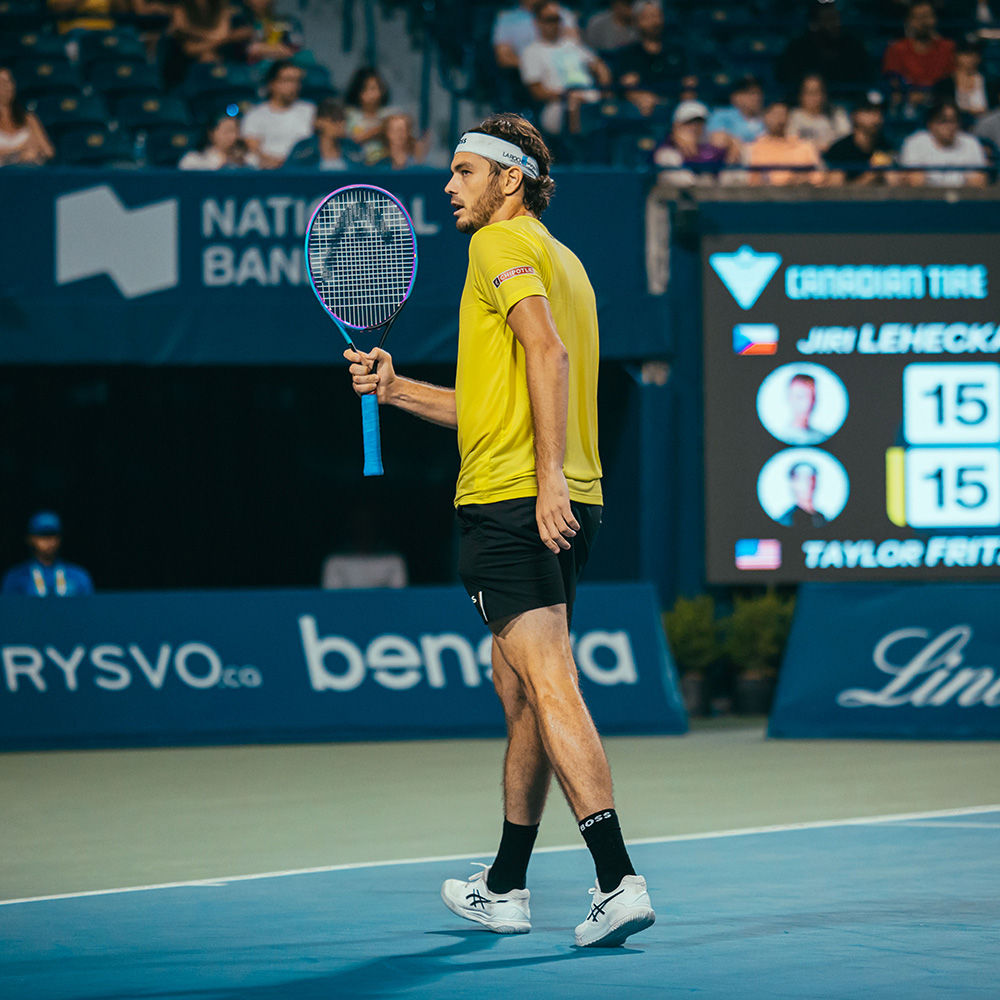 Taylor Fritz waves his tennis racquet celebrating a point while wearing bright yellow and black at the Canada Open