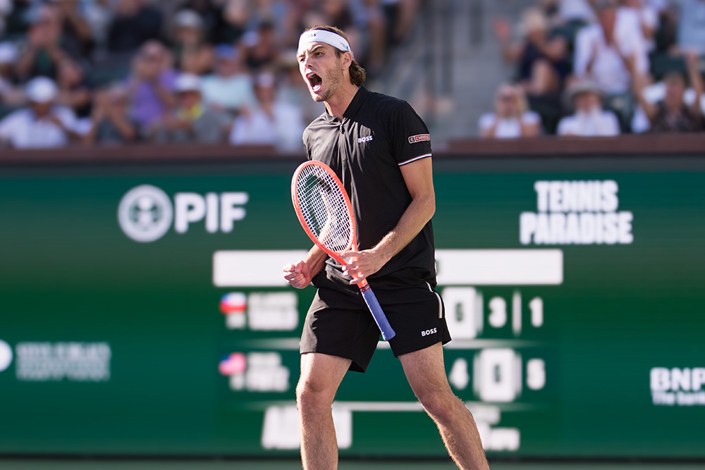 Taylor Fritz raises his orange tennis racquet in triumph, celebrating a victory at the 2025 BNP Paribas Open.