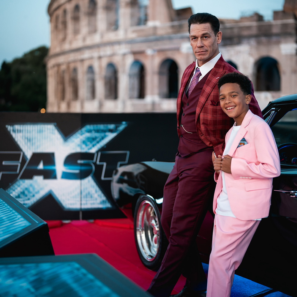 John Cena and Leo Abelo Perry lean against a car while posing for a photo at the Fast X movie premiere.