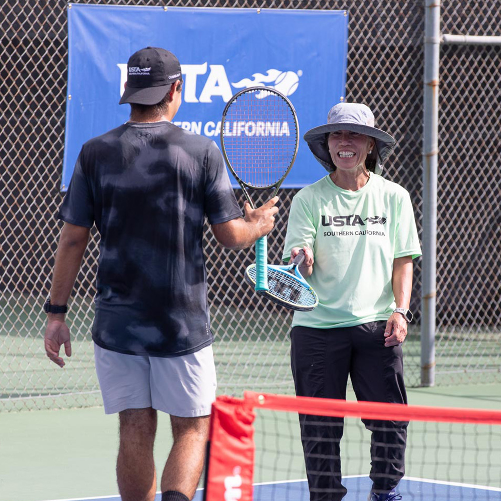Judy Dean smiles while tapping racquets with a fellow player at Marguerite Tennis Pavilion during the 2025 USTA Community Social.