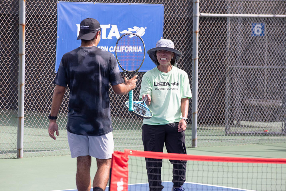 Judy Dean smiles while tapping racquets with a fellow player at Marguerite Tennis Pavilion during the 2025 USTA Community Social.