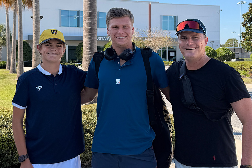 From left to right, Vincent MacAllister, professional tennis player Jenson Brooksby, and Chad MacAllister, pose together for a photo on a sunny outdoor path.