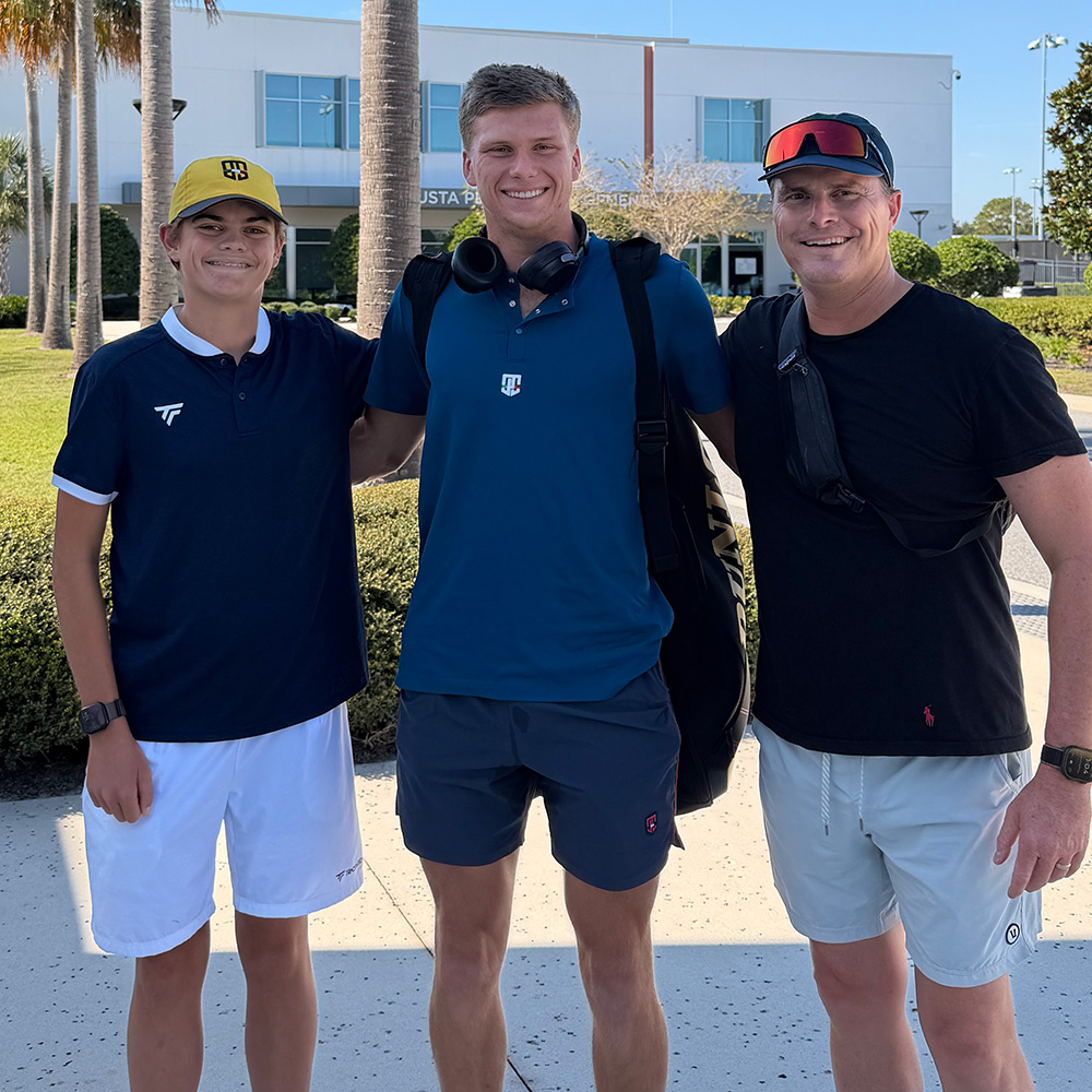 From left to right, Vincent MacAllister, professional tennis player Jenson Brooksby, and Chad MacAllister, pose together for a photo on a sunny outdoor path.