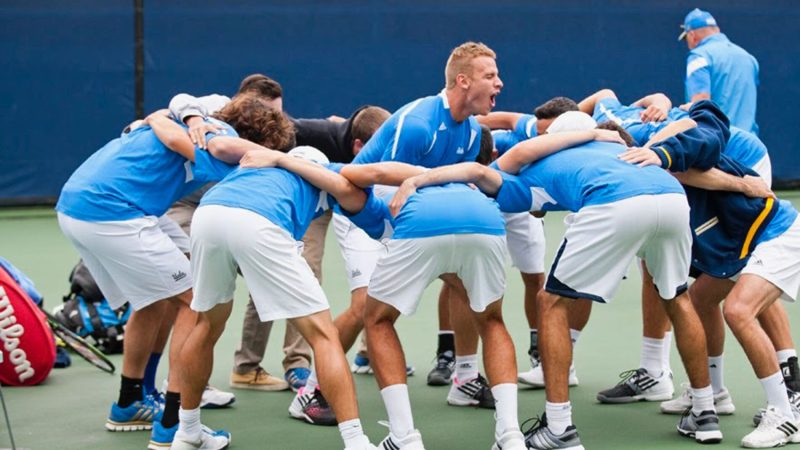 Karue Sell in the middle of a team huddle during a UCLA men's tennis match