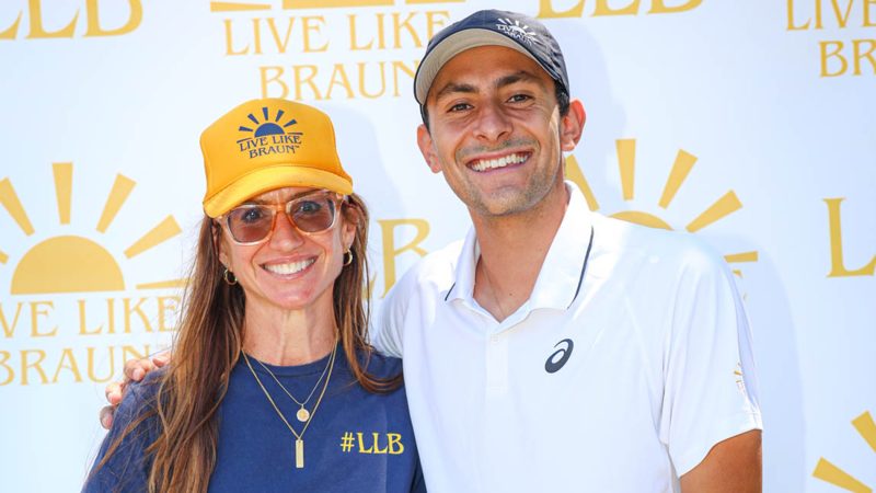 Jennifer Levi and Emilio Nava smile in front of a Live Like Braun Foundation backdrop at the second annual Live Like Braun (LLB) Memorial Tennis Tournament.